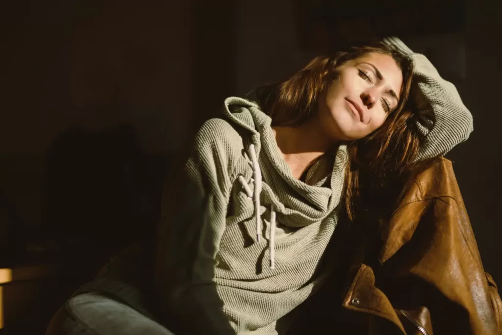 Détente et relaxation : une femme sereine en position de détente, baignée par la lumière douce. Les traits apaisés, une expression de calme intérieur. Un moment de quiétude et de bien-être.